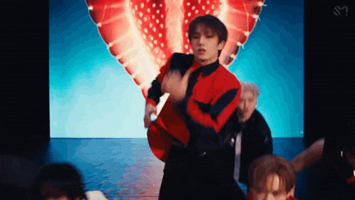 a man in a red jacket is dancing on a stage in front of a strawberry heart .