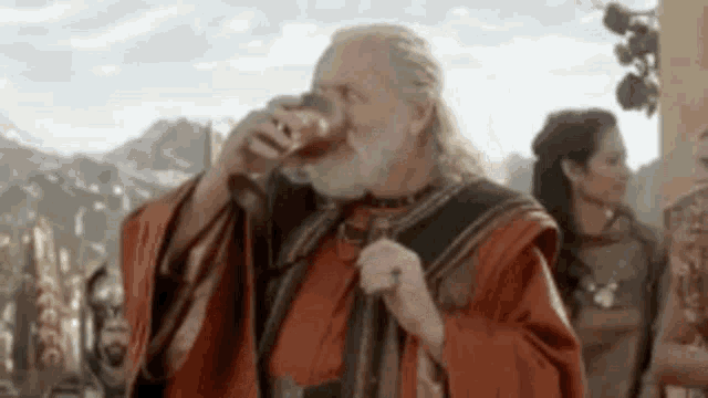 a man with a beard and a red robe is drinking from a cup .