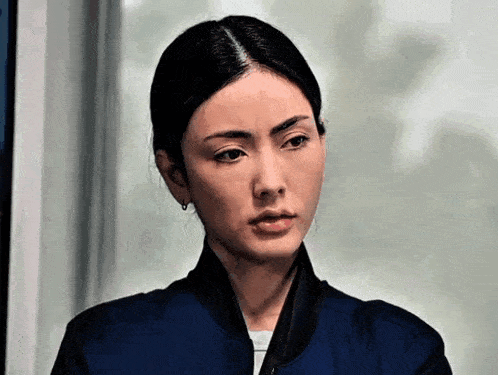 a woman in a blue jacket is making a funny face and looking at the camera .