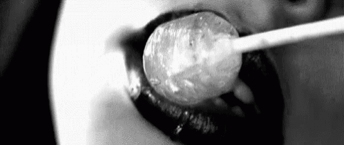 a black and white photo of a woman licking a lollipop .