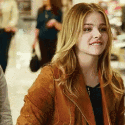 a woman is wearing a brown jacket and smiling while walking in a store .