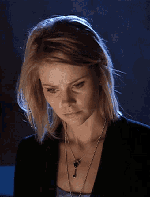 a woman wearing a necklace with a key on it looks down