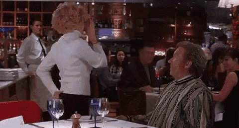 a man is sitting at a table in a restaurant while a woman stands in front of him .