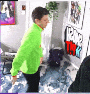 a man in a neon green jacket is dancing in a room with a sign that says h2om2