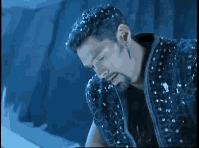 a man with a beard is wearing a black vest with sequins on it and a piercing in his ear .