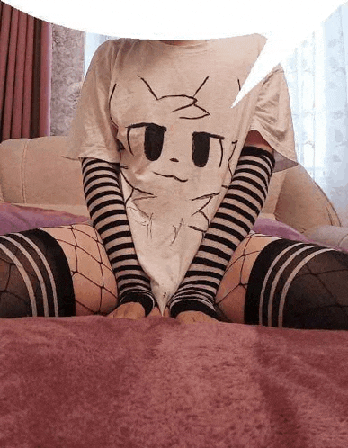 a woman is sitting on a bed wearing a t-shirt with a cat on it and striped socks .