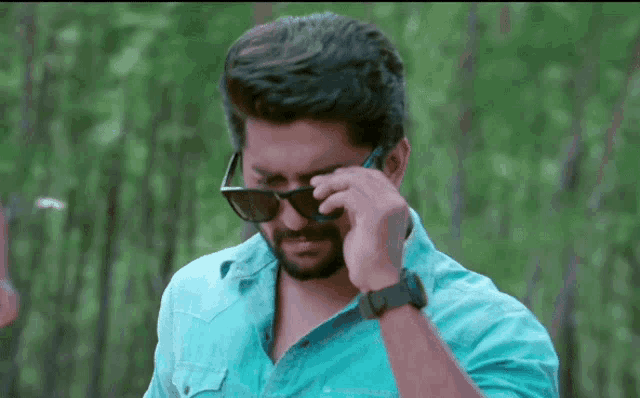 a man wearing sunglasses and a blue shirt talks on a cell phone