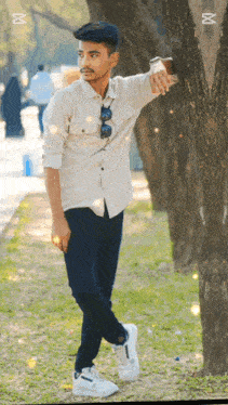 a young man leans against a tree in a park while taking a picture of himself