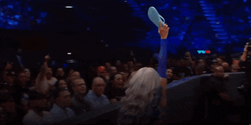 a woman in a blue shirt is holding up a blue item in front of a crowd