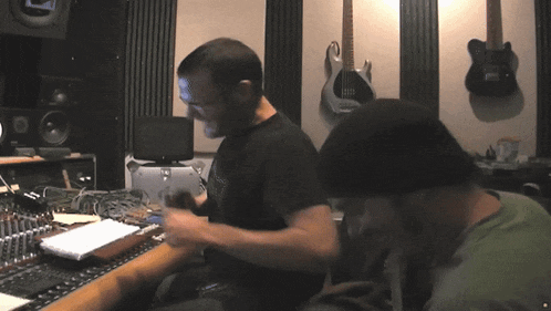 two men are working in a recording studio with guitars hanging on the wall behind them