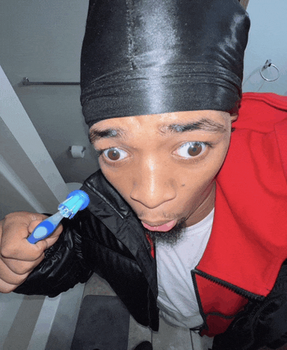 a man wearing a black hat and a red jacket is holding a toothbrush