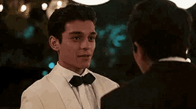 a man in a tuxedo and bow tie is talking to another man in a tuxedo .
