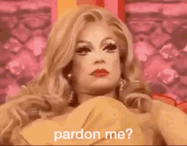 a drag queen is sitting on a couch and saying `` pardon me ? '' .