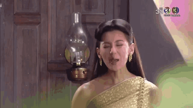 a woman in a gold dress is making a face in front of a lamp .