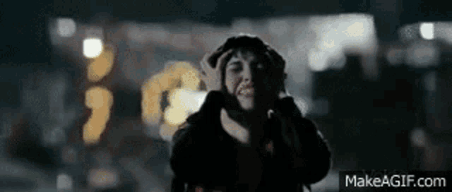 a woman is covering her ears with her hands while standing in front of a building at night .