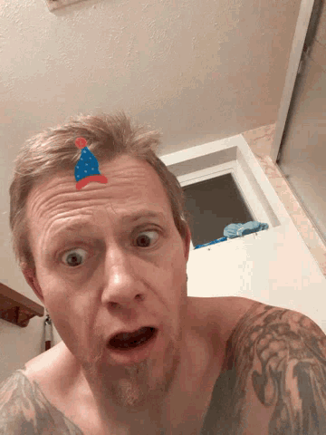 a shirtless man with a birthday hat on his forehead looks surprised