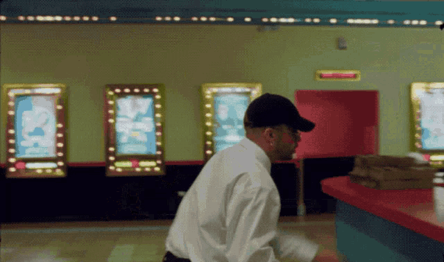 a man in a white shirt and black hat is standing in front of a sign that says ' exit ' on it