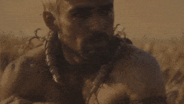 a man with a beard and a necklace is laying in a field of tall grass .