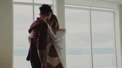 a man and a woman are kissing in front of a window in a room .