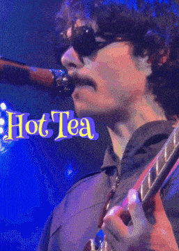 a man singing into a microphone and playing a guitar with the words hot tea behind him