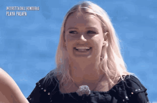 a blonde woman is smiling in front of a blue sky with the words in diretta dall honduras playa palapa