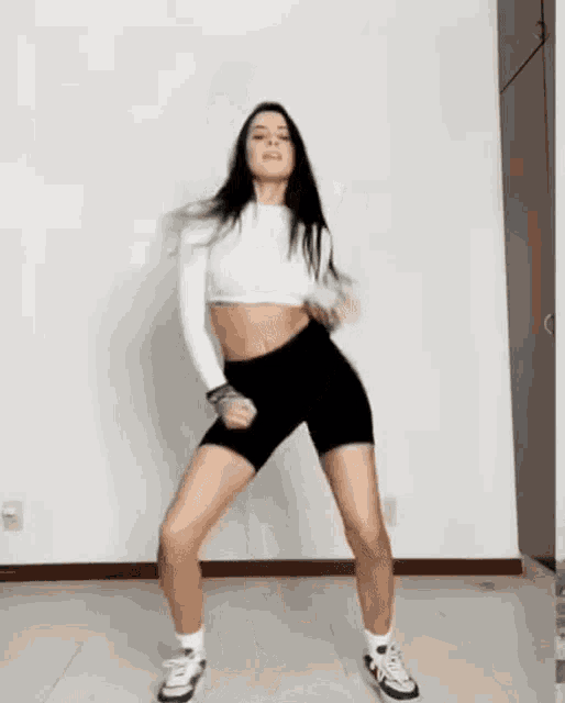 a woman is dancing in a room wearing shorts and a crop top .