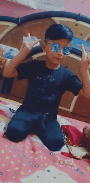 a young boy wearing sunglasses is sitting on a bed and making a peace sign
