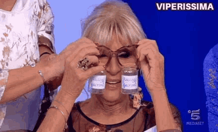 a woman wearing glasses is holding two small bottles in front of her face and the words viperissima are above her