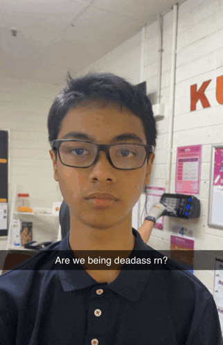 a young man wearing glasses stands in front of a wall that says kc