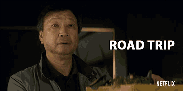 a man stands in front of a sign that says " road trip "
