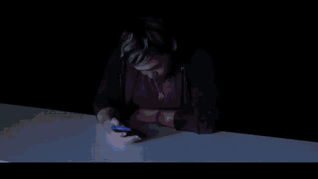 a man in a red shirt and black jacket is sitting at a table in the dark