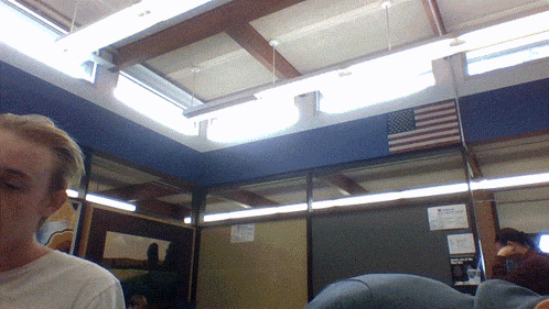 a man in a white shirt stands in a room with an american flag on the wall