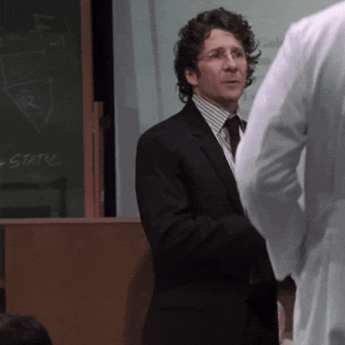a man in a suit stands in front of a blackboard that says static on it