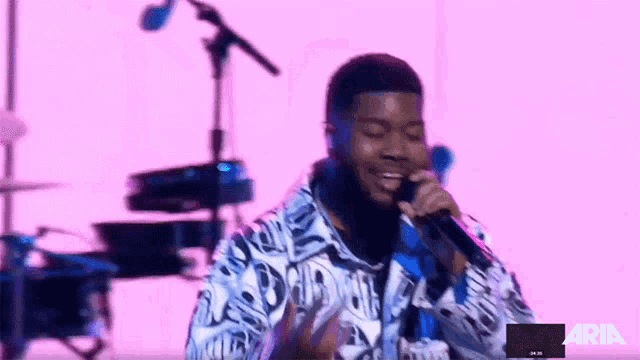 a man singing into a microphone in front of a pink background with the word aria on it