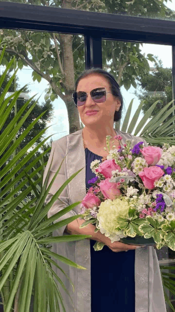 a woman wearing sunglasses holds a bouquet of flowers in her hands