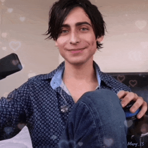 a young man in a blue shirt is smiling and holding a remote control in his hand