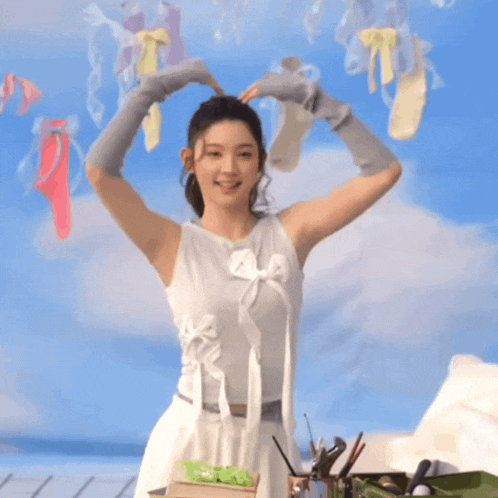 a woman making a heart shape with her hands in front of a wall with clothes hanging on it