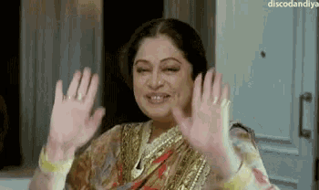 a woman in a sari is waving her hands in the air and smiling .