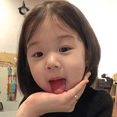 a little girl is sticking her tongue out while holding her chin