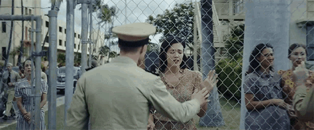 a woman behind a chain link fence is talking to a man in a uniform