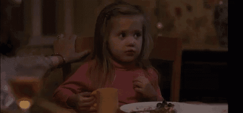 a young girl is sitting at a table with a plate of food .