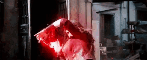 scarlet witch is standing in a dark room with a red light coming out of her eyes .