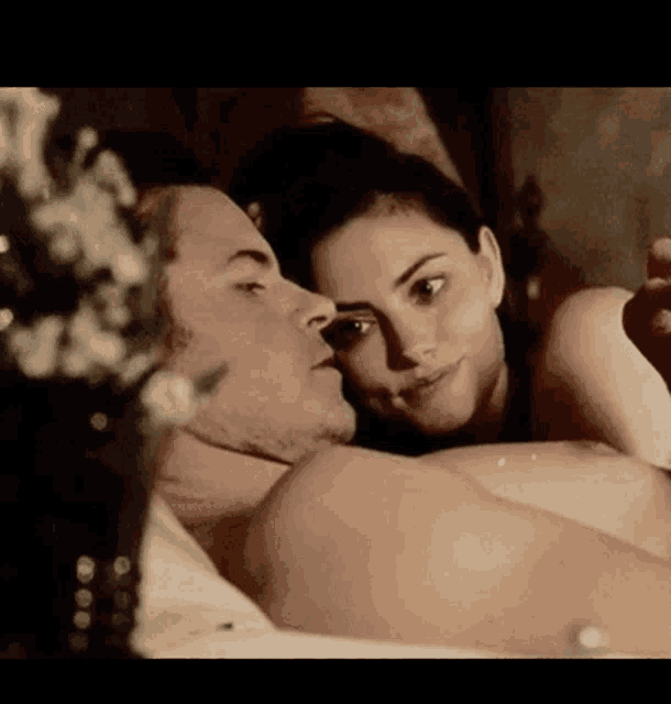 a man and a woman are laying in bed and the woman is kissing the man on the forehead .