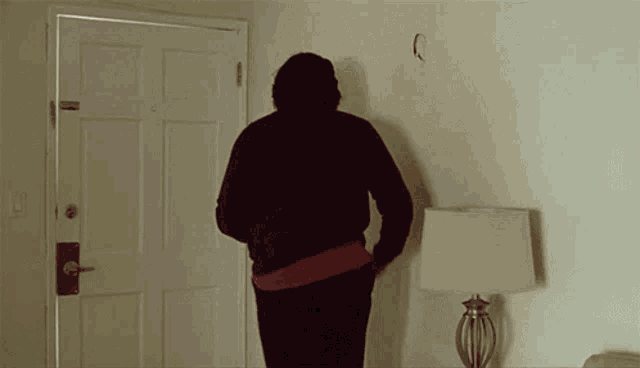 a man in a red sweater is standing in front of a door with a lamp in front of him