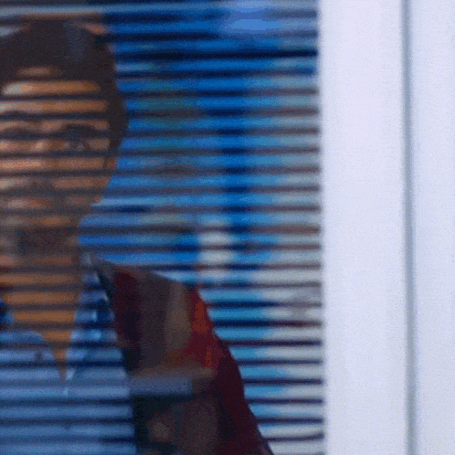 a man looking through a window with blinds on it