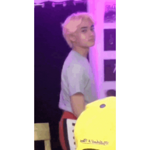 a young man with blonde hair is standing in a room with a yellow hat .