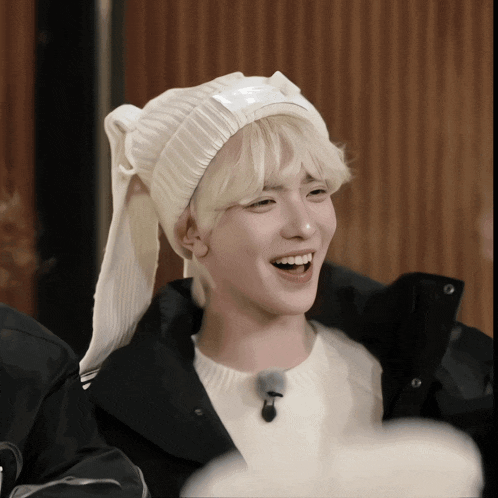 a young man wearing a white hat and a black jacket smiles