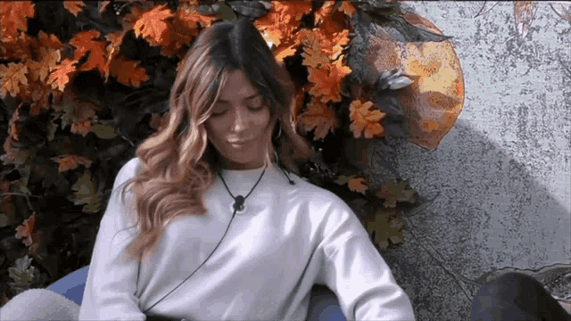 a woman in a white sweater is sitting in front of a bunch of flowers