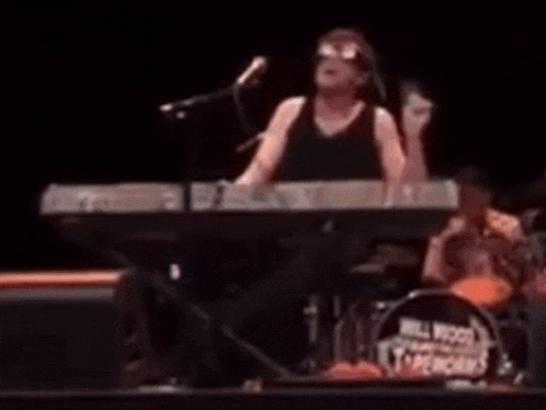 a man singing into a microphone while playing a keyboard in front of a drum set that says bill wood 's