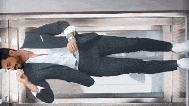 a man in a suit and white shirt is standing upside down in an elevator